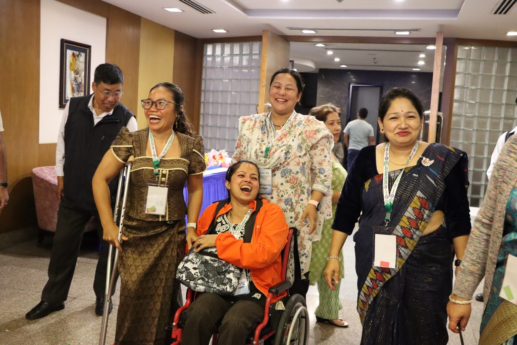 Four Asian women are laughing; one is in a wheelchair, one walks with crutches.